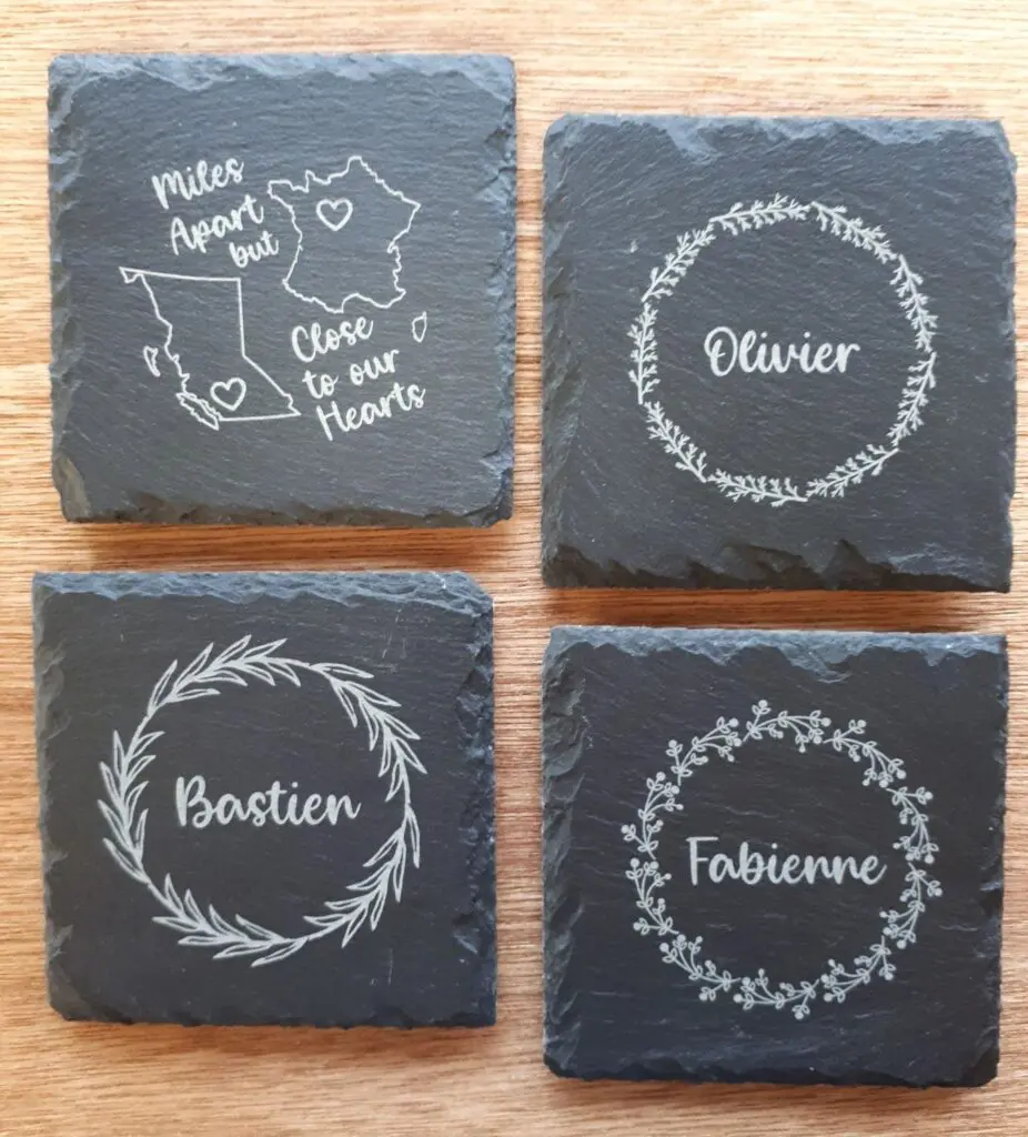 Four slate coasters with decorative white floral designs and names.
