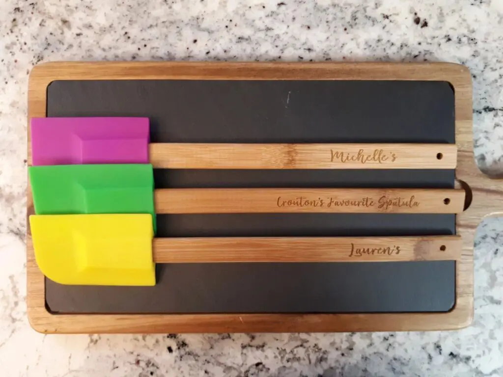 Three wooden spatulas with colorful silicone heads on a dark tray.